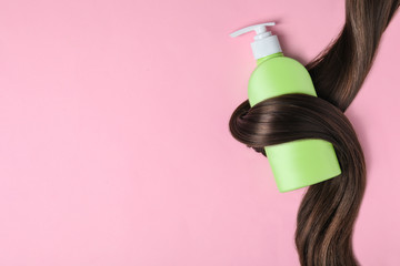 Shampoo bottle wrapped in lock of hair on pink background, flat lay with space for text. Natural...