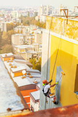 Industrial rope access worker hanging from the building while painting the exterior facade wall....