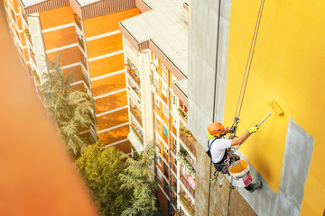 Industrial rope access worker hanging from the building while painting the exterior facade wall. Industrial alpinism concept image. Top view