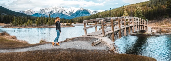 Girl in leather jacket about to cross bridge infront of mountains