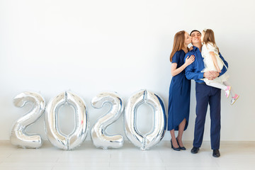 Young happy family mother and father and daughter standing near balloons shaped like numbers 2020...