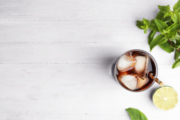 Glass of refreshing soda drink with ice cubes, mint and lime on white wooden table, flat lay. Space...