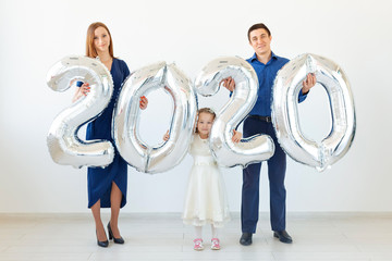 Young happy family mother and father and daughter holding balloons shaped like numbers 2020 on...