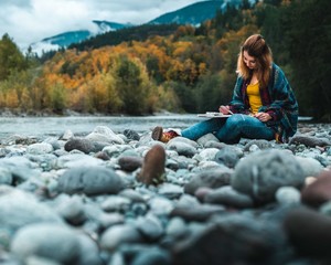 Girl on rocky beach drawing in book on fall day