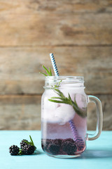 Mason jar of blackberry lemonade on blue table against wooden background. Space for text