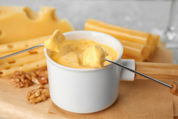 Pot of tasty cheese fondue and fork with bread on cutting board