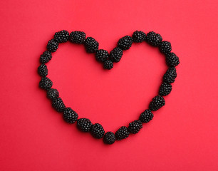 Obraz premium Heart shaped frame made of fresh blackberries on red background, top view. Space for text
