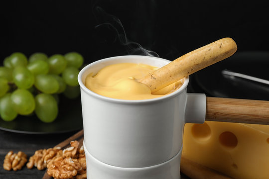 Pot Of Tasty Cheese Fondue And Bread Stick On Black Wooden Table