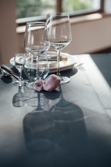 Glasses, flowers, fork, knife served for dinner in restaurant with cozy interior,