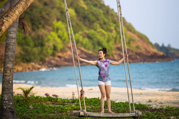 Asian girl swinging on a swing on a tropical beach.