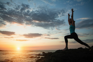 Fototapeta na wymiar Fitness woman practicing yoga on the ocean coast during a sunset.