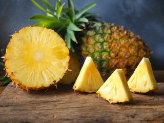 Fototapeta na wymiar Ripe pineapple fruit cut in half and triangle shape on a rustic wooden table for high fiber fruits concept.