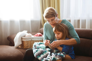 elderly woman  teaching her granddaughter to knit at home. the grandmother spends time together in...