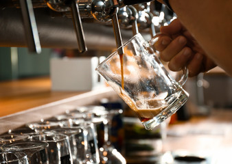 Bartender pouring beer into glass in pub, closeup