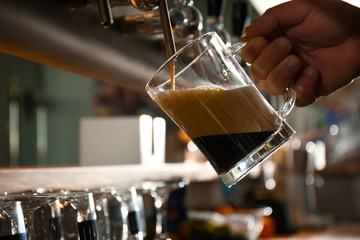 Fototapeta na wymiar Bartender pouring beer into glass in pub, closeup