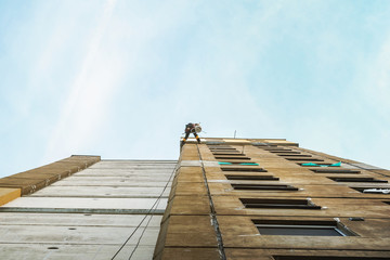 Industrial rope access worker hanging from the building while painting the exterior facade wall. Industrial alpinism concept image. Top view