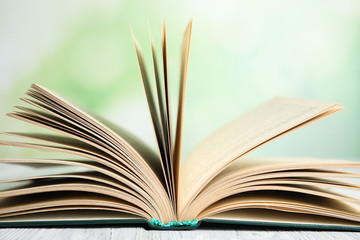 Open book on white wooden table against blurred green background, closeup