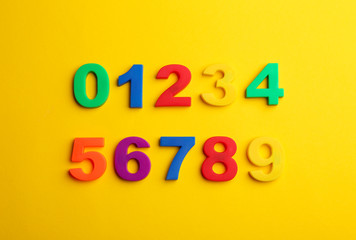 Colorful magnetic numbers on yellow background, flat lay