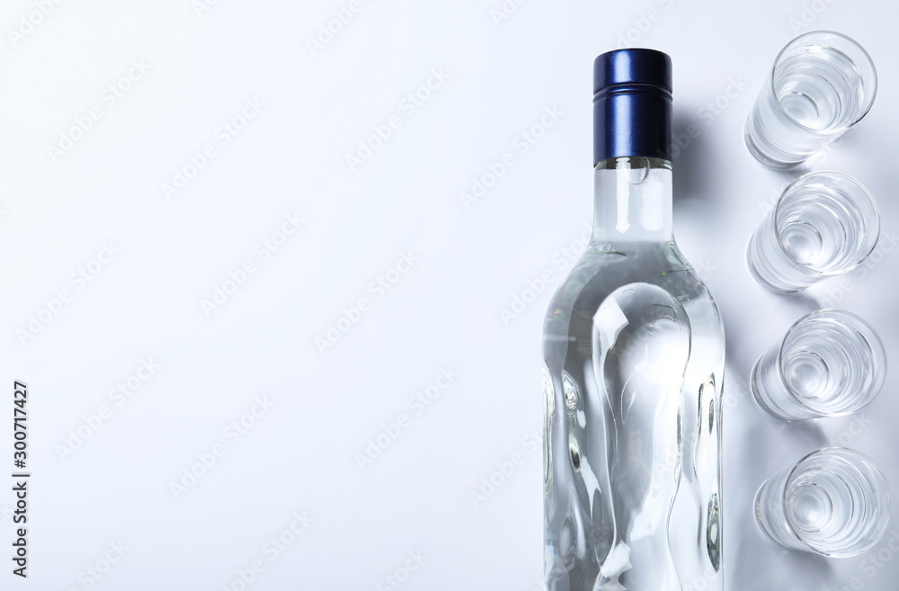 Sticker Bottle of vodka and shot glasses on white background, flat lay. Space for text