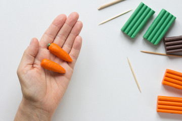 Two handmade small carrots made from polymer clay on woman hand on white background