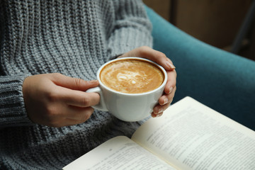 Woman with cup of coffee reading book at home, closeup