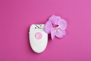 Modern epilator and flower on purple background, flat lay