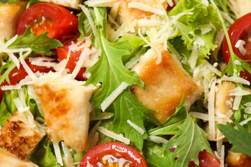 Delicious Caesar salad with fresh ingredients as background, closeup