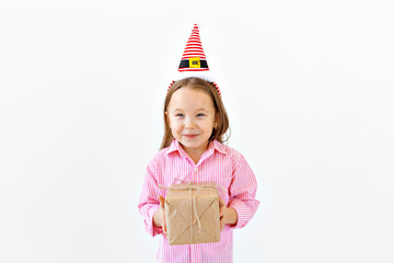 Smiling funny child in Santa red hat holding gift box in hand over white background with copyspace. Christmas concept.