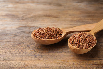 Buckwheat grains in spoons on wooden table
