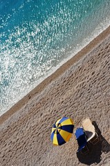 beautiful seascape background, a yellow-blue umbrella and two sun loungers on the beach of Porto Katsiki on Lefkada Island. sea view, social distance on the beach