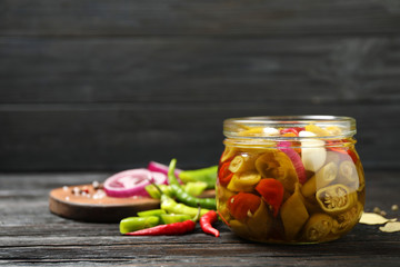 Glass jar with pickled peppers on wooden table. Space for text