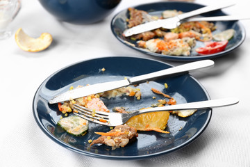 Plate with food leftovers on white tablecloth after party, closeup