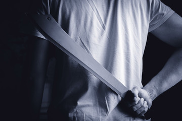 a man holds a machete in hand behind - obrazy, fototapety, plakaty