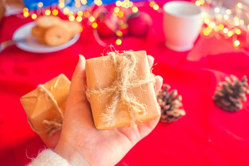 New Year and Christmas present in a box in craft paper in the hands of a young woman on a red background