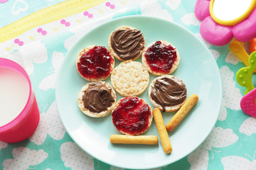 Food art idea. Wheat round bread rolls with jam and chocolate paste in the shape of a flower on a blue plate. Milk and a toy...