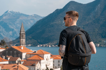 Fototapeta na wymiar Young stylish man traveler with big backpack enjoying of old european town of Montenegro view