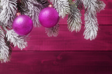 Pink Christmas balls on spruce frosty brunches over wooden background