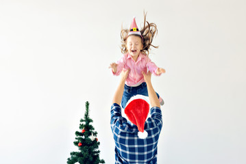 Christmas, holidays and fatherhood concept - Funny dad wearing santa hat throws his daughter up on white background with copy space