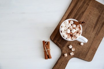Top view mugs with hot chocolate and marshmallows on chopping board near cinnamon.