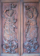 Da Nang, Vietnam - March 10, 2019: Chua An Long Chinese Buddhist Temple. Closeup of Fierce armed male defenders carved on brown door to santuary. 