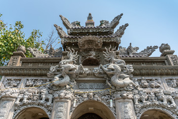 Da Nang, Vietnam - March 10, 2019: Chua An Long Chinese Buddhist Temple. Fisheye on Gray stone Pagoda entrance and roof structure of sanctuary under light blue sky and with green foliage.