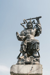 Obraz premium Da Nang, Vietnam - March 10, 2019: Chua An Long Chinese Buddhist Temple. Closeup of bronze statue of fiece sword fighting knight on corner of roof against blue sky. 