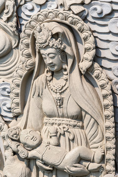 Da Nang, Vietnam - March 10, 2019: Chua An Long Chinese Buddhist Temple. Closeup of Gray stone happy Bodhisattva with child fresco as backdrop for Guan Yin statue, not in picture.
