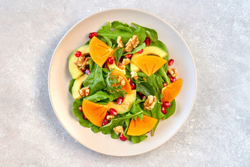 Salad with arugula, persimmon, avocado, pomegranate seeds and walnuts