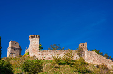 Fototapeta na wymiar Assisi ancient medieval walls ruins at the top of the town with blue sky above