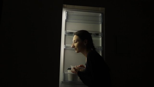 Hungry Woman with eating disorder Looking in a Fridge Taking Food at Night. Concept of unhealthy lifestyle