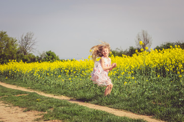 Fototapeta premium little charming girl in summer dress running in rural path in green nature