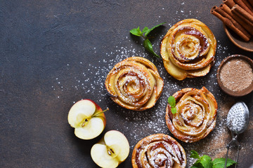 Dish of apple roses baked in puff pastry on a dark concrete background with apples. View from above - 300735437