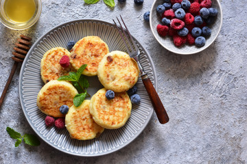 Cheesecakes with berries and honey for breakfast on a gray concrete background. View from above.
