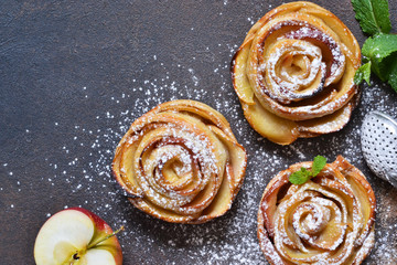Dish of apple roses baked in puff pastry on a dark concrete background with apples. View from above